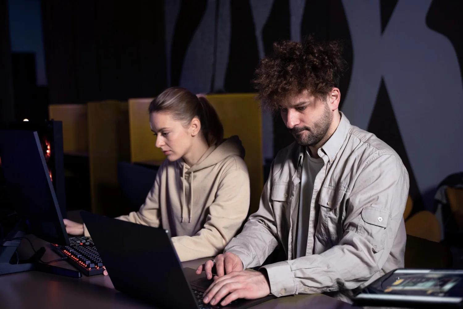 Two focused IT professionals working on laptops in a dimly lit, modern workspace, representing the efficiency of IT staffing solutions in providing skilled tech talent for businesses needing expert support.